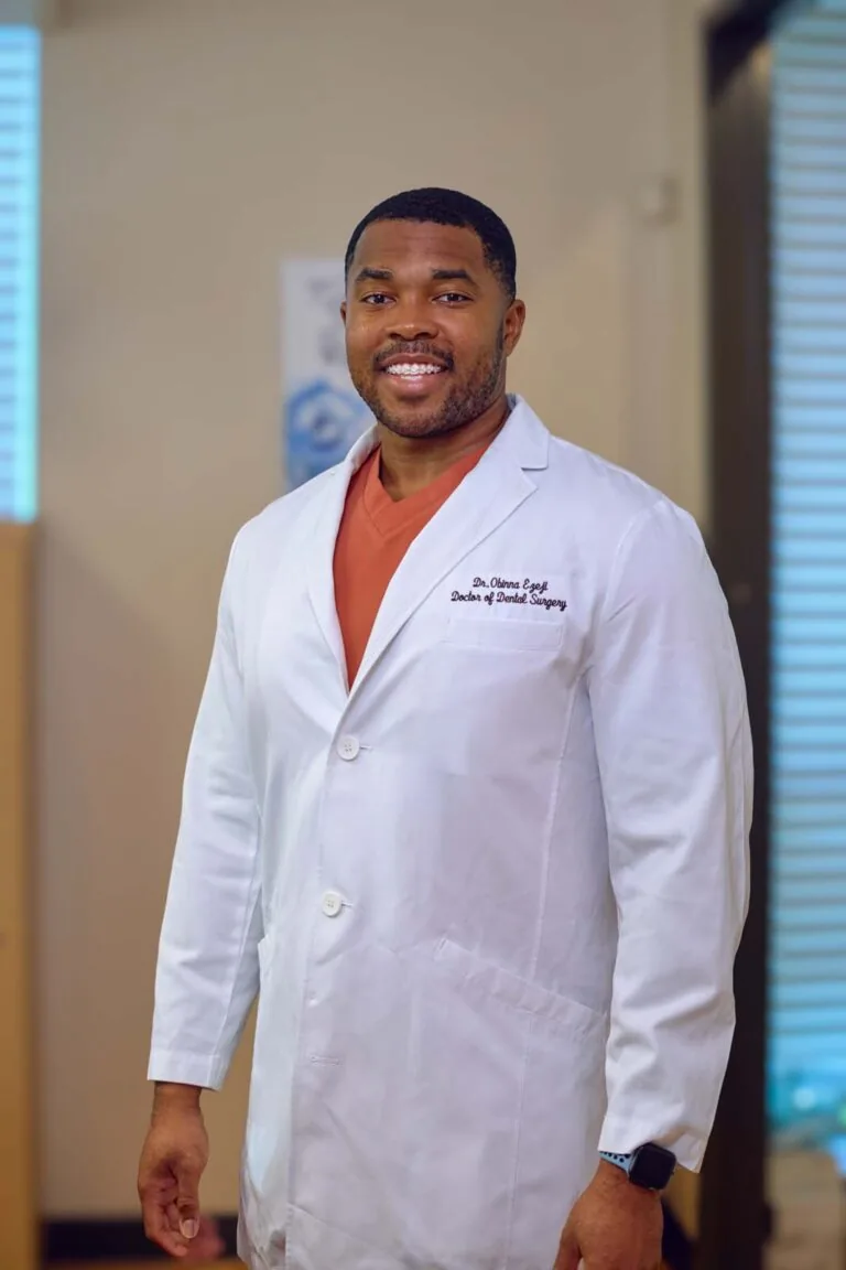 Smiling dentist in a white coat standing confidently in a clinic.