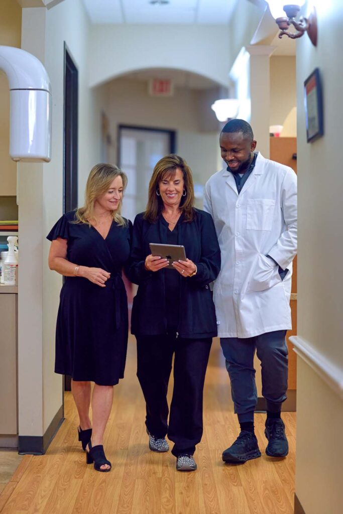 Three dental professionals walking together while reviewing information on a tablet.